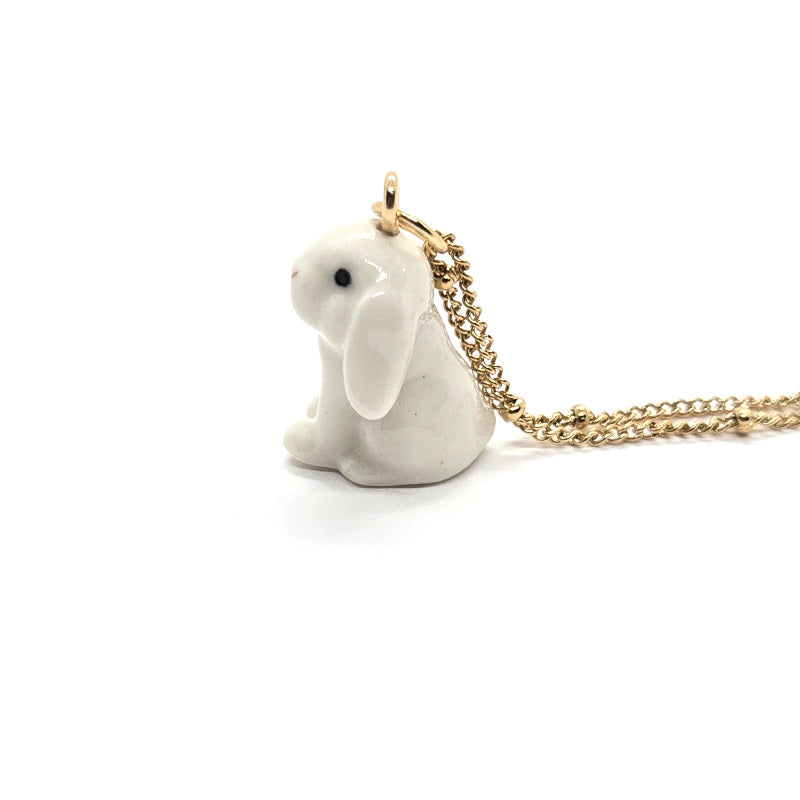 Left side view of ceramic white lop rabbit pendant attached to gold-plated beaded chain.