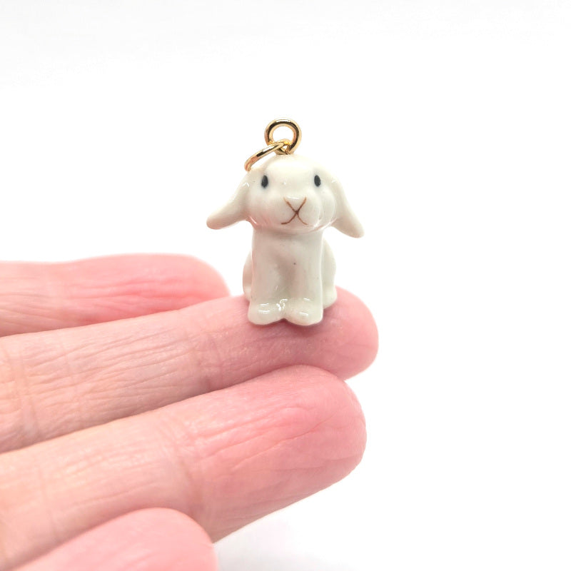 Ceramic white lop rabbit pendant on a finger for scale.