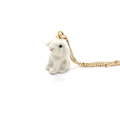 Side view of ceramic white lop rabbit pendant attached to gold-plated beaded chain.